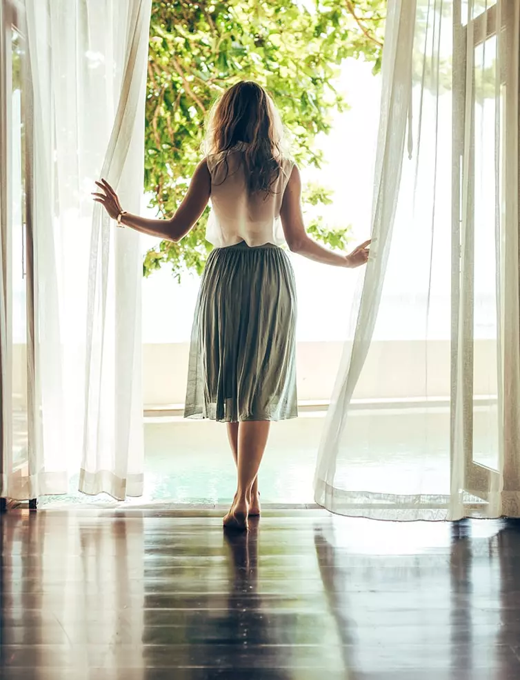 the backside of a women wearing a pleated skirt looking through a floor to ceiling window